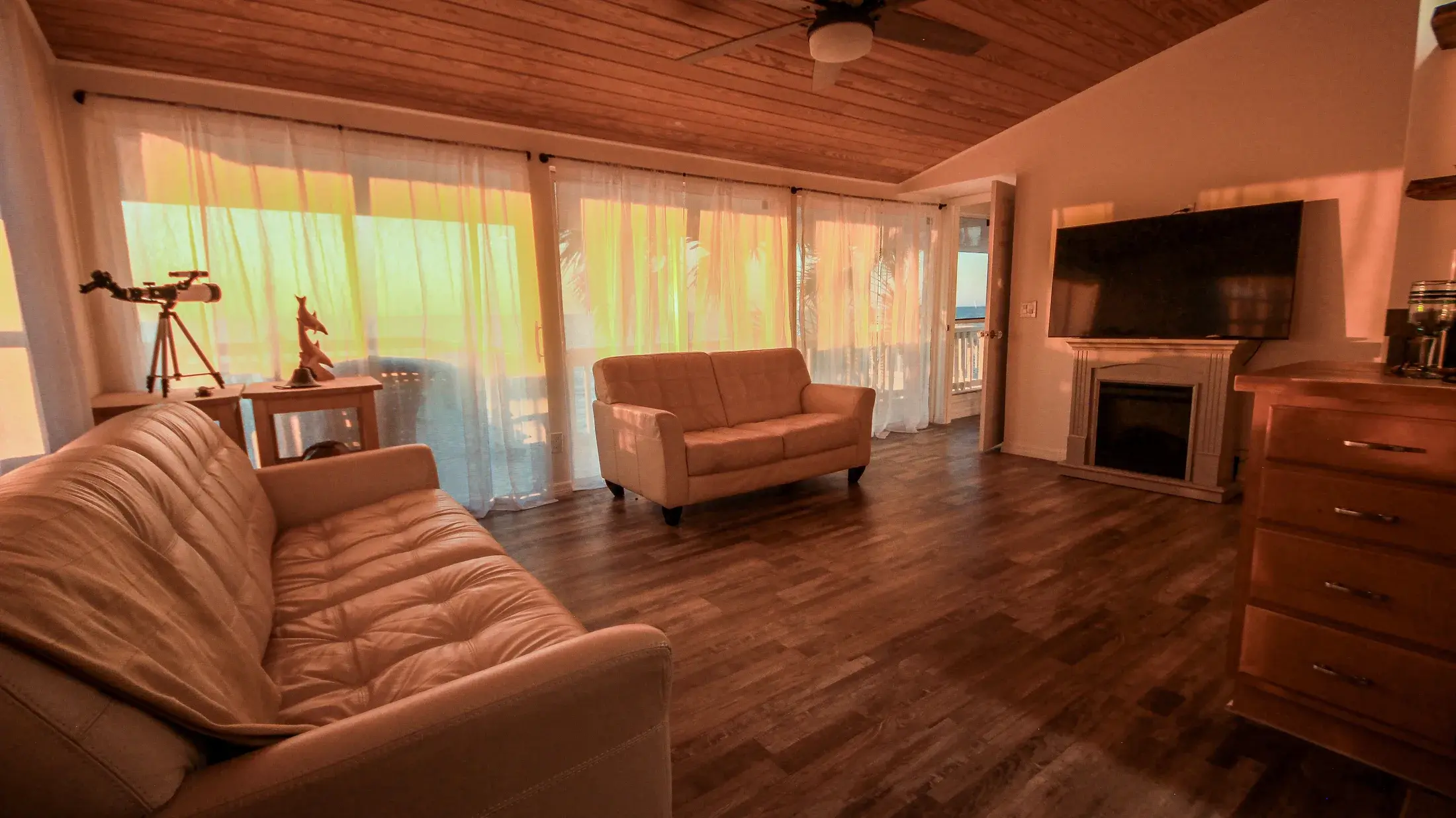 Living room with couches, electric fireplace, and wall-mounted TV facing the Gulf side windows.