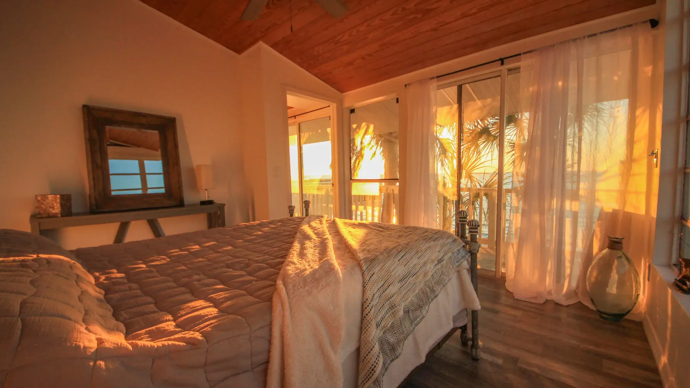 Primary bedroom at sunset with curtains glowing and water visible outside.